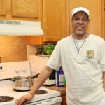 Male VOA client stands smiling by a stove in his Permanent Supportive Housing apartment.