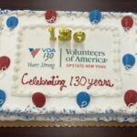 Cake with "Celebrating 130 years" with VOA logo and candles.