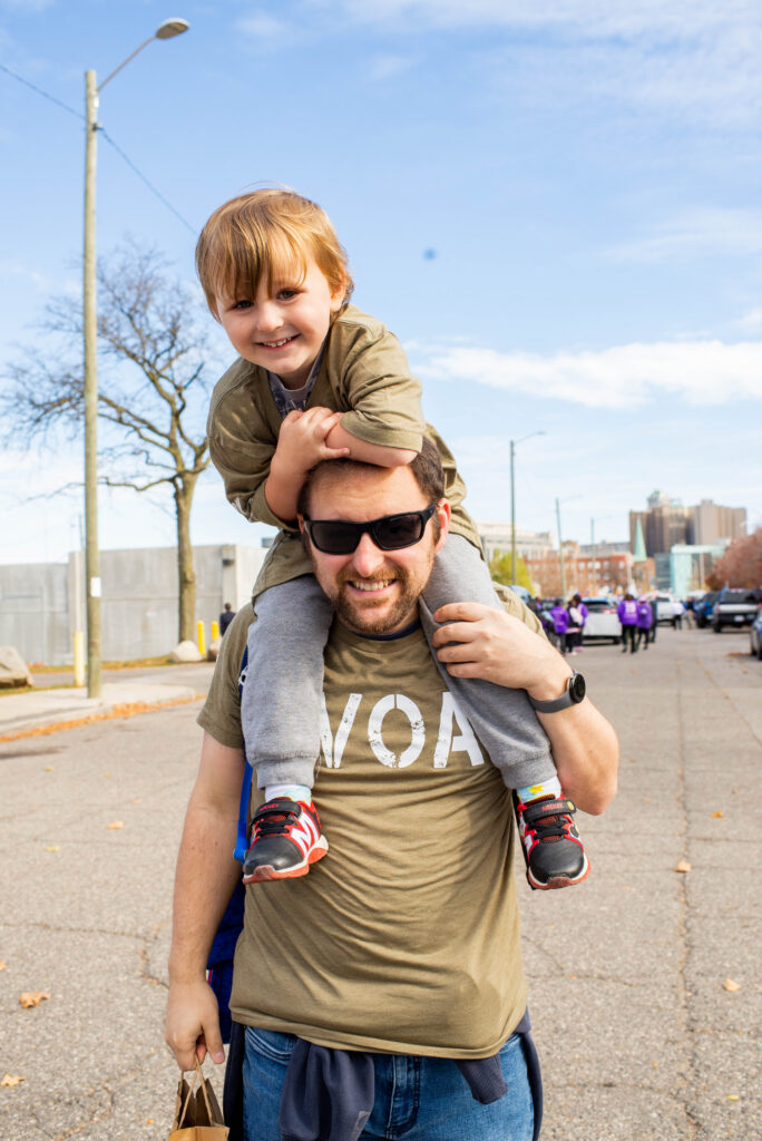 Father wearing sunglasses has smiling toddler son on his shoulders.
