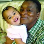 Father hugs infant daughter. Both smiling towards the camera.