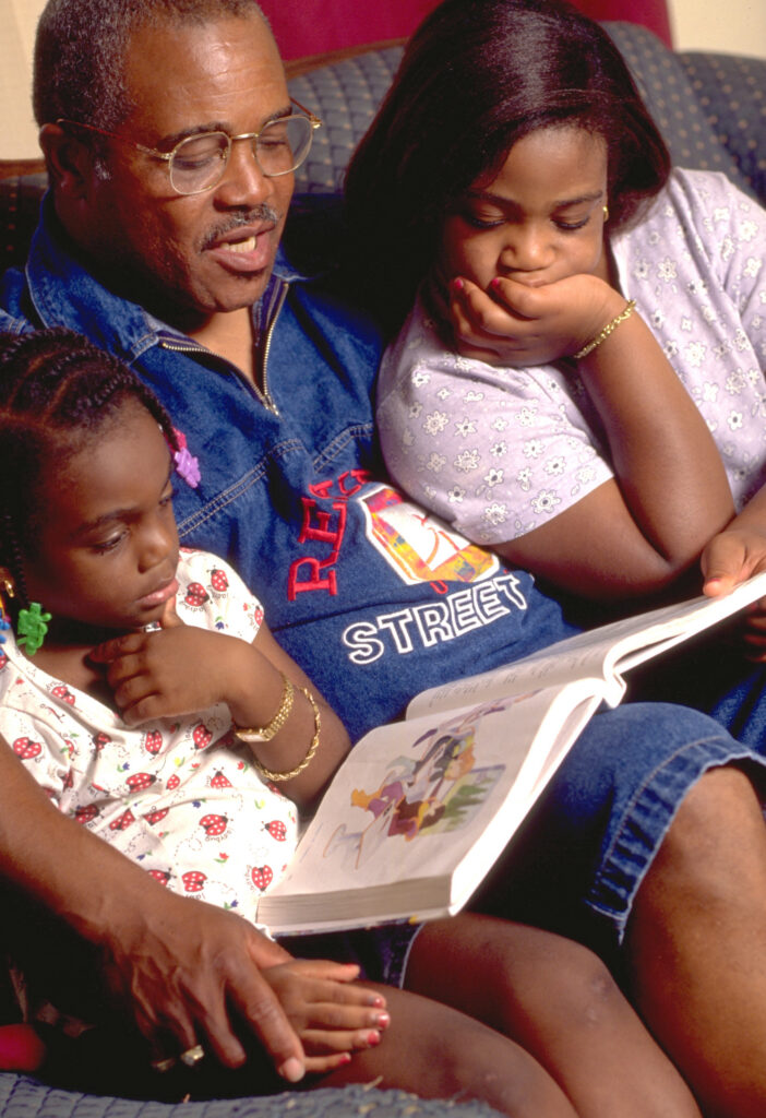 Father sits between two daughters and reads them a book.