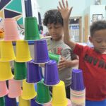 Two school-age children build a tower with colorful plastic cups.
